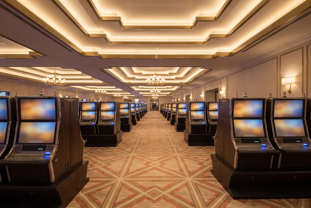 A quiet casino floor in the evening: rows of glowing cabinets along a patterned carpet under a stepped cream and brass ceiling